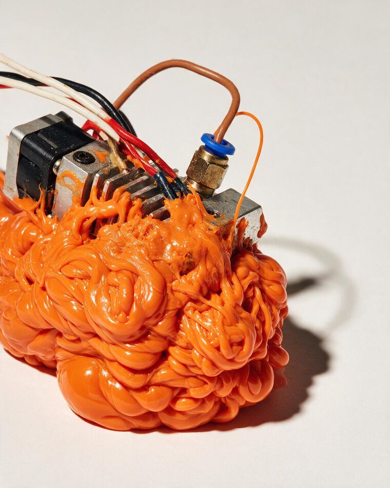 A printer hotend completely encased in a hardened orange blob of melted filament