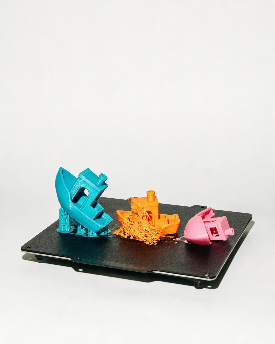 Three 3DBenchy test boats on a print bed, each one printed badly enough to collapse